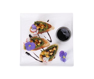 Photo of Delicious bruschettas with pesto sauce, tomatoes, balsamic vinegar and violet flowers isolated on white, top view
