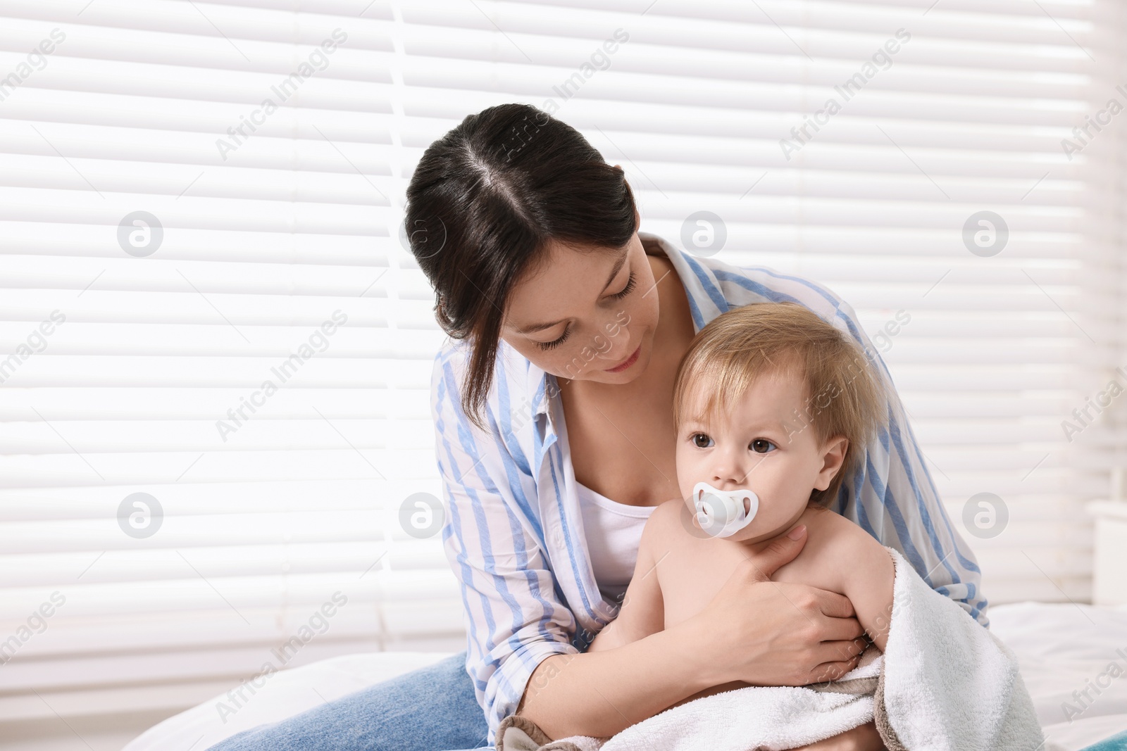 Photo of Mother wrapping her cute little baby with towel after bathing on bed