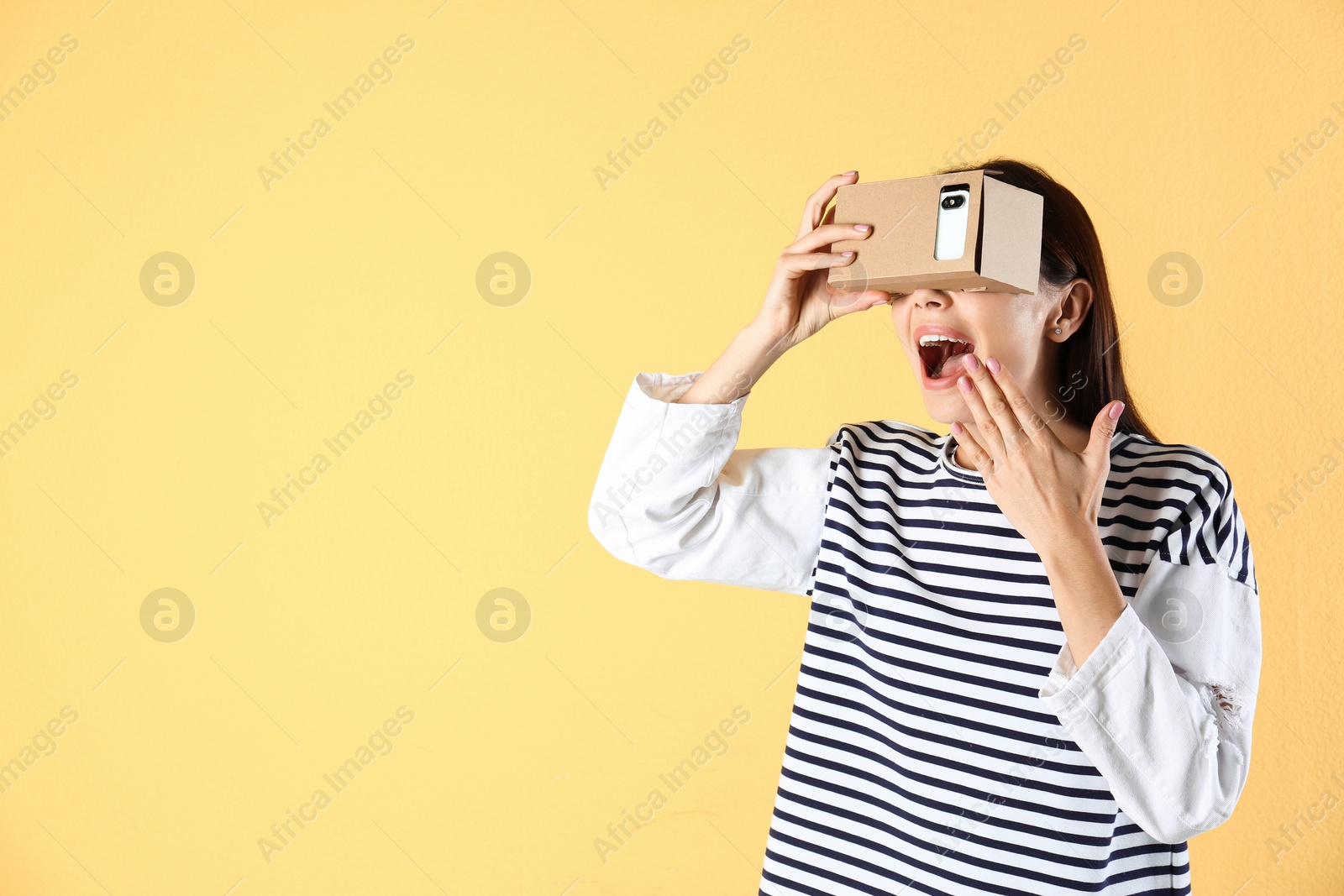 Photo of Young woman using cardboard virtual reality headset on color background. Space for text