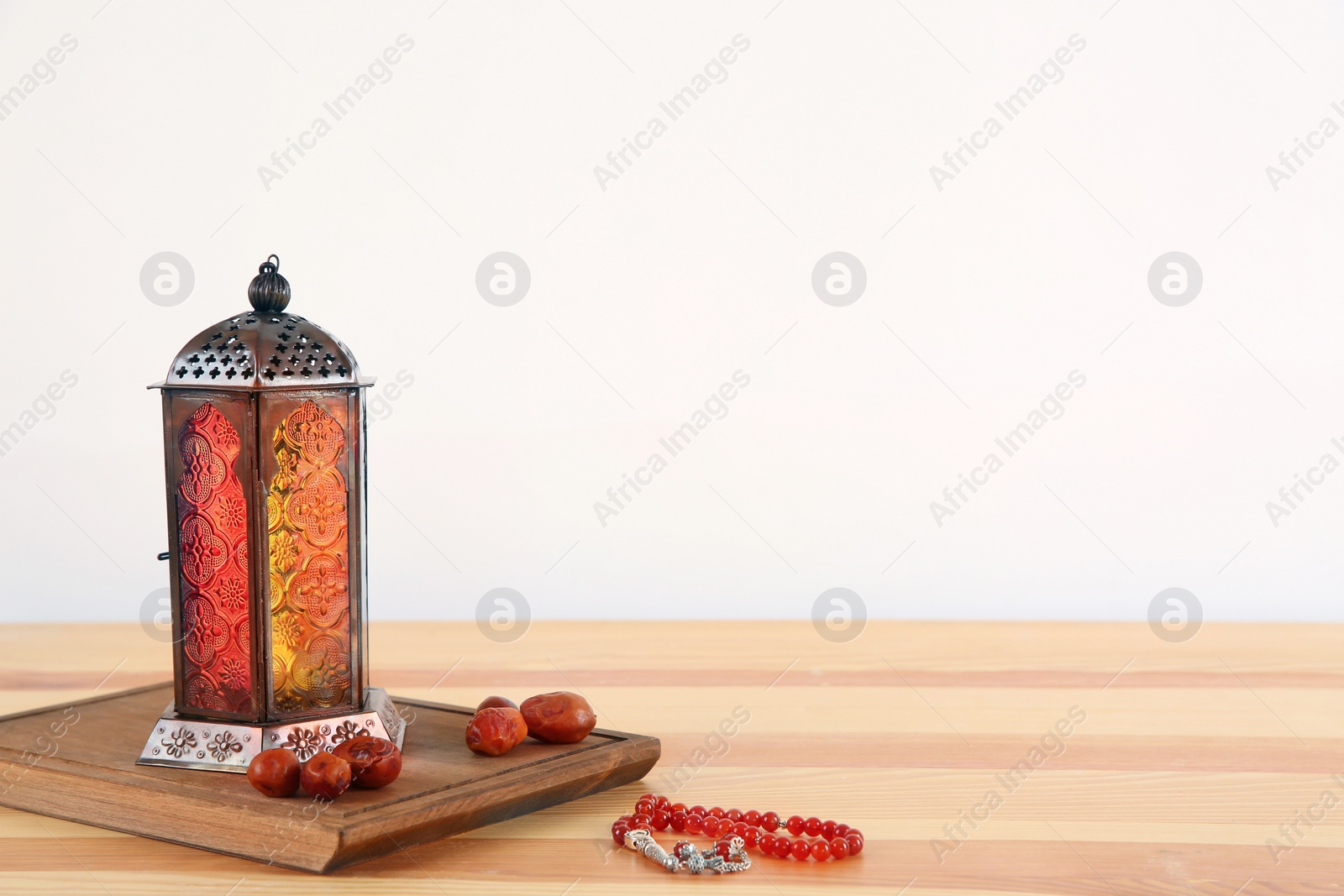 Photo of Muslim lantern Fanous, dried dates and prayer beads on table against light background. Space for text