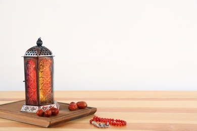 Photo of Muslim lantern Fanous, dried dates and prayer beads on table against light background. Space for text