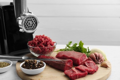 Photo of Meat grinder, beef, onion, garlic, parsley and spices on white wooden table, space for text