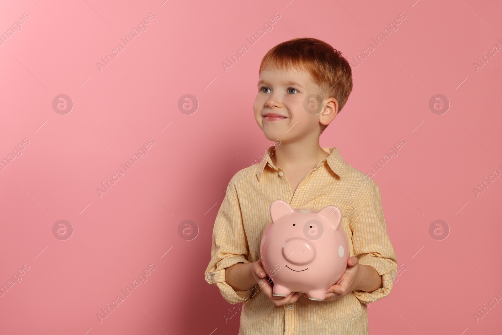 Photo of Cute little boy with ceramic piggy bank on pale pink background, space for text