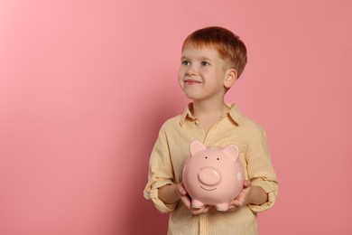 Cute little boy with ceramic piggy bank on pale pink background, space for text
