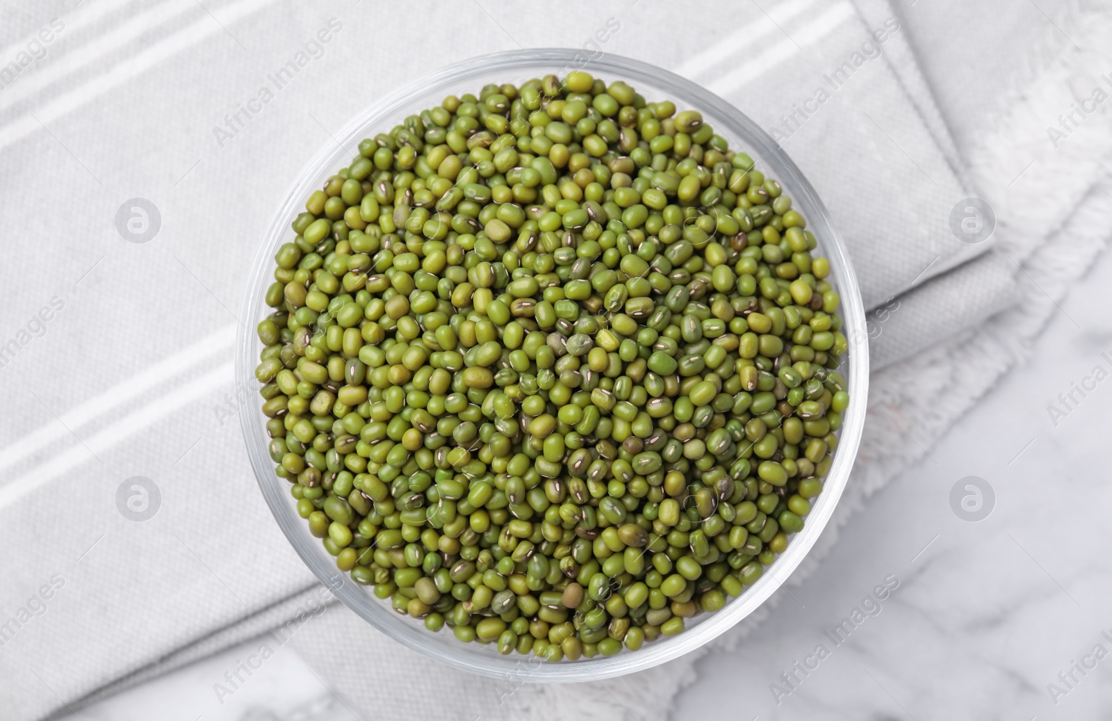 Photo of Glass bowl with green mung beans on white marble table, top view