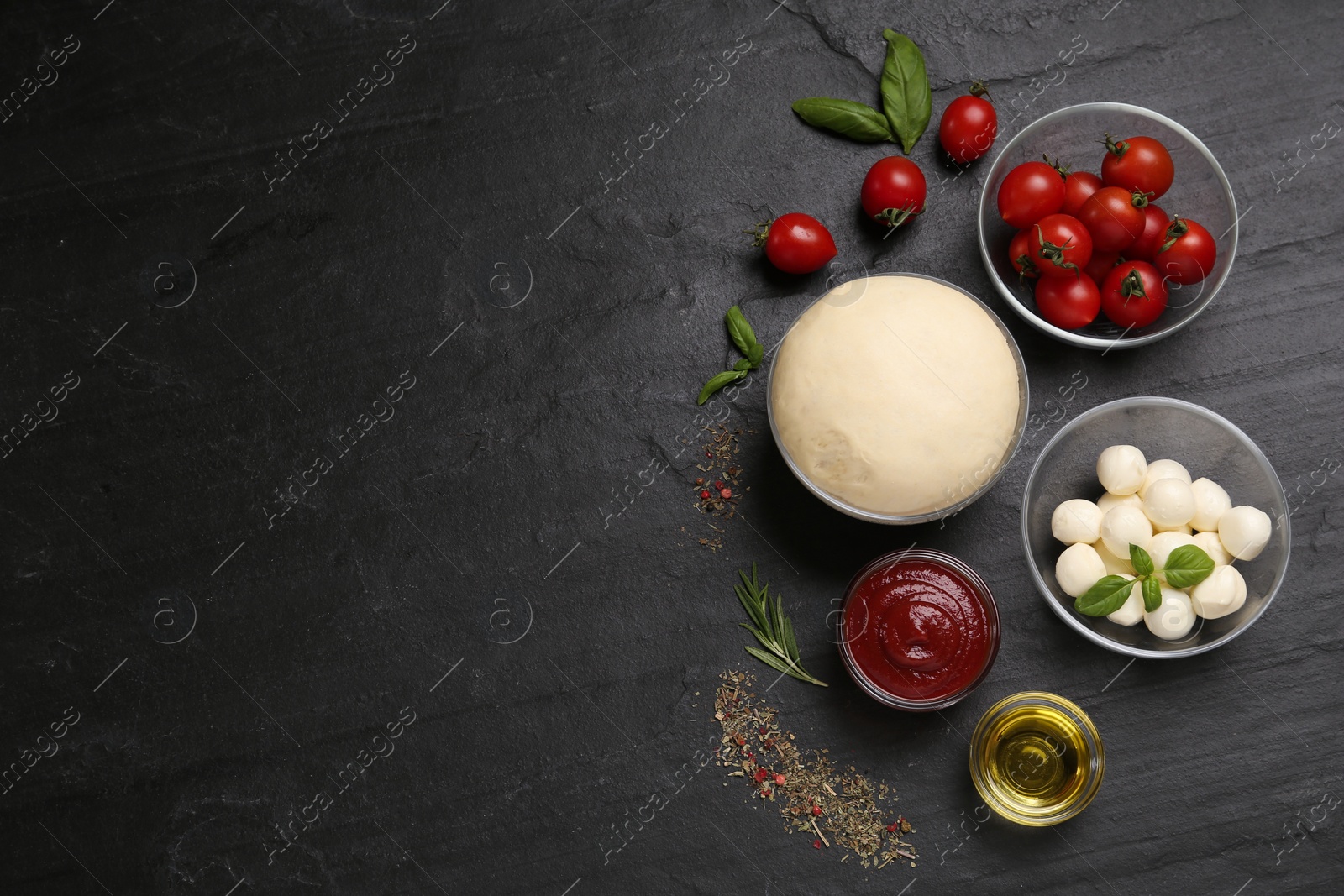 Photo of Raw pizza dough and other ingredients on black table, flat lay. Space for text