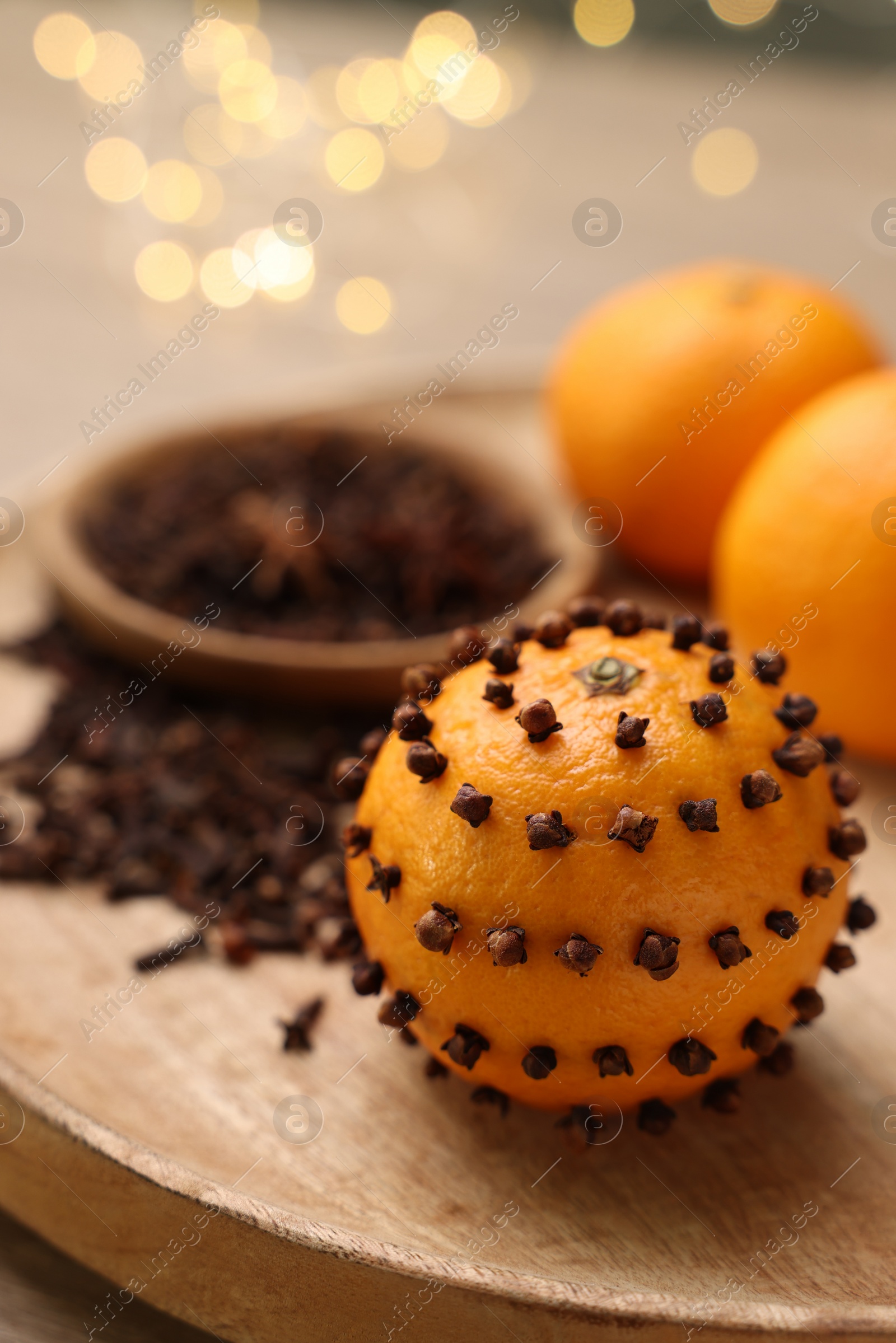 Photo of Pomander ball made of tangerine with cloves on wooden table against blurred festive lights, closeup