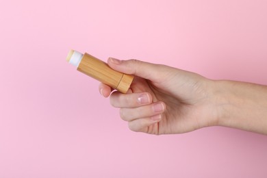 Woman with lip balm on pink background, closeup