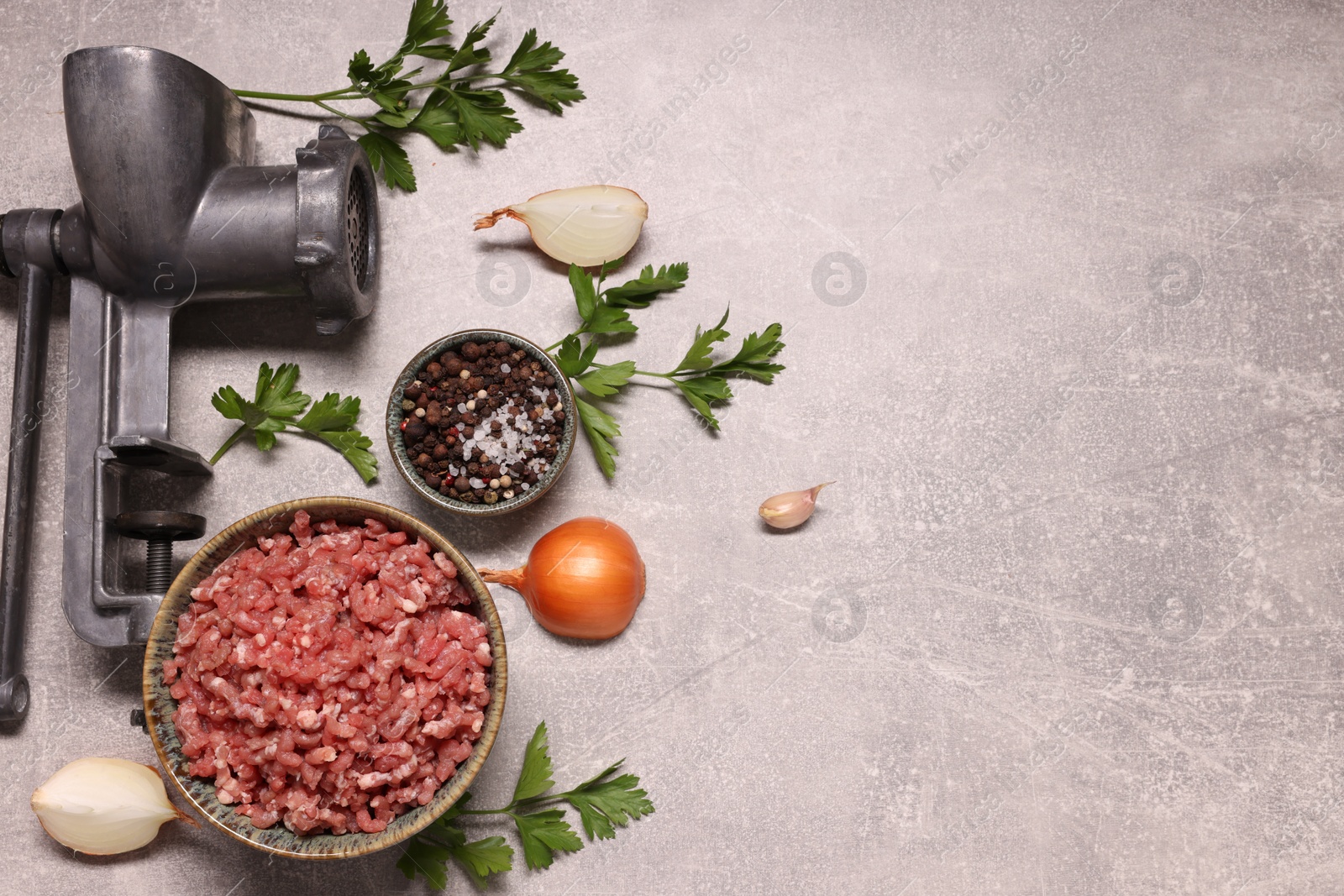 Photo of Manual meat grinder, beef mince, peppercorns, onion and parsley on light grey table, flat lay. Space for text