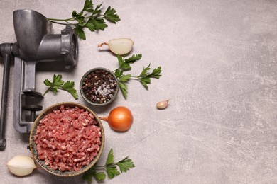 Photo of Manual meat grinder, beef mince, peppercorns, onion and parsley on light grey table, flat lay. Space for text