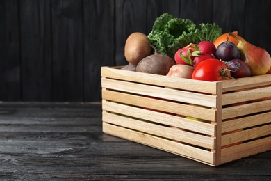 Crate full of different vegetables and fruits on black wooden table, space for text. Harvesting time