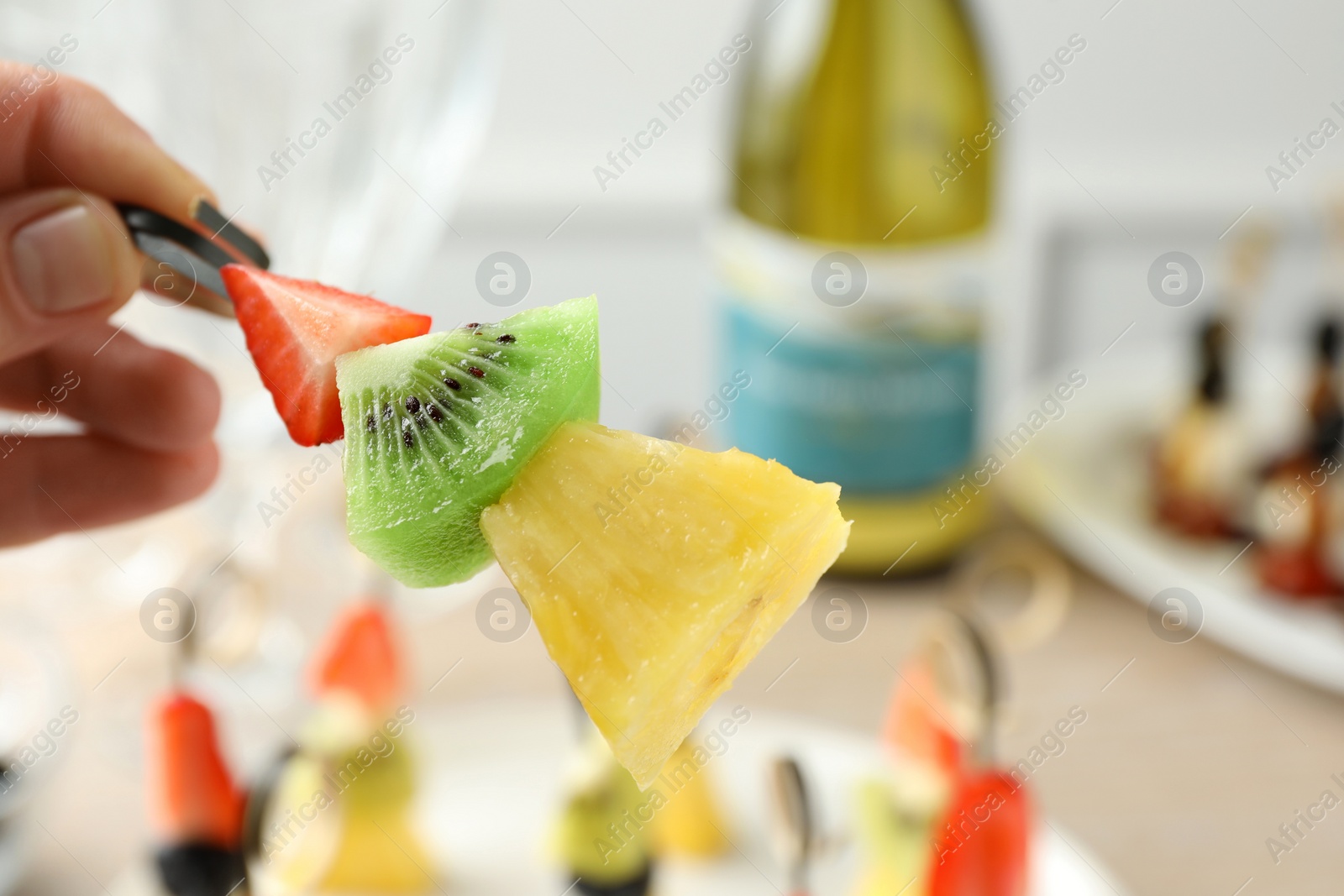 Photo of Woman holding tasty canape with pineapple, kiwi and strawberry at table, closeup