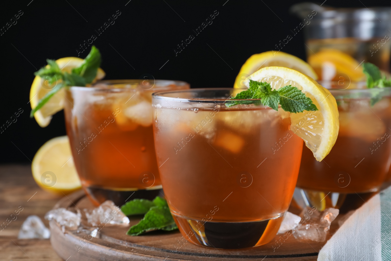 Photo of Delicious iced tea on wooden table against black background