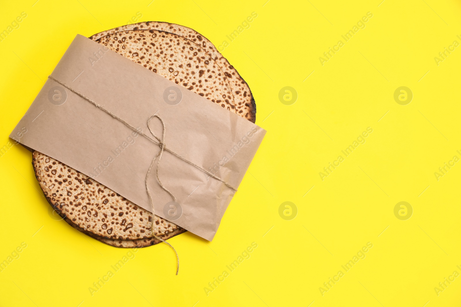 Photo of Top view of tasty matzos wrapped with paper on yellow background, space for text. Passover (Pesach) celebration