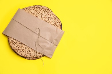 Photo of Top view of tasty matzos wrapped with paper on yellow background, space for text. Passover (Pesach) celebration