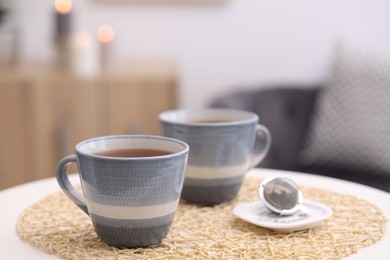 Photo of Cups of tea and snap infuser with dry leaves on white table indoors