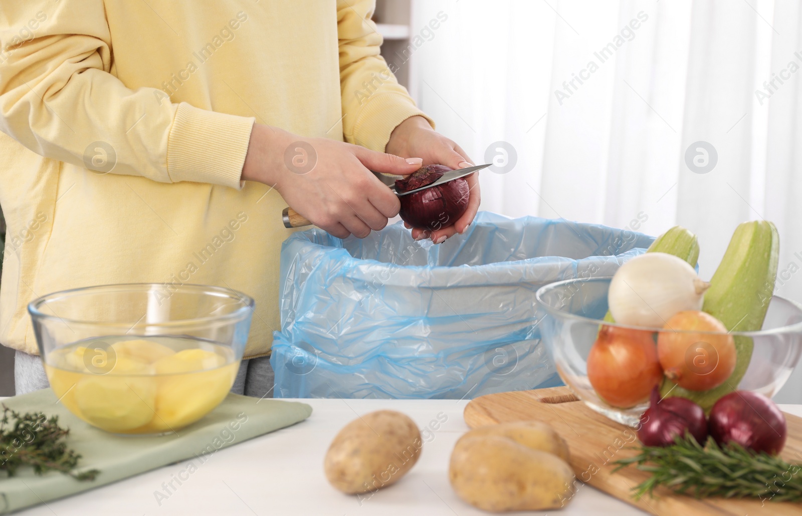 Photo of Woman peeling fresh onion above garbage bin indoors, closeup