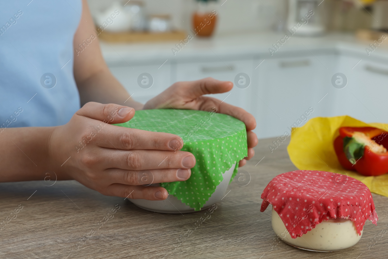 Photo of Woman holding bowl covered with beeswax food wrap at wooden table in kitchen, closeup