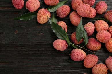 Photo of Fresh ripe lychee fruits on dark wooden table, flat lay. Space for text