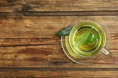 Cup of aromatic green tea on wooden table, top view. Space for text