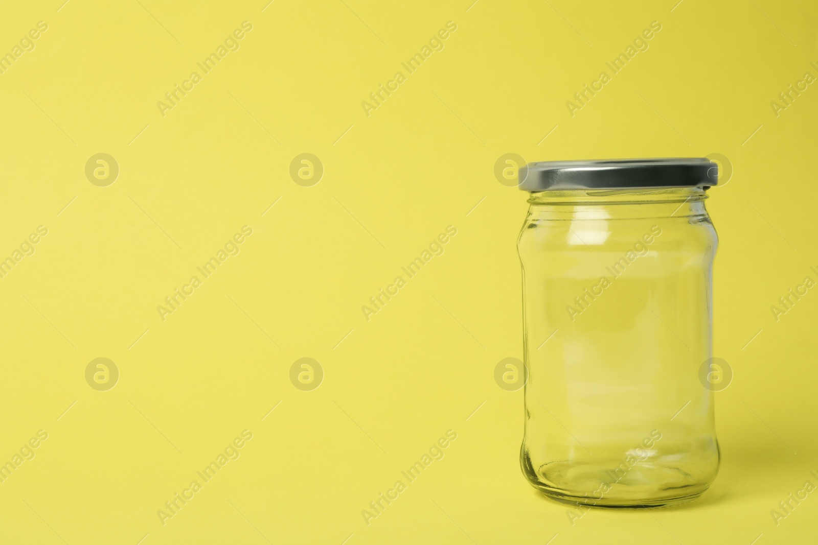 Photo of Closed empty glass jar on light yellow background, space for text