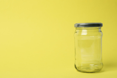 Closed empty glass jar on light yellow background, space for text