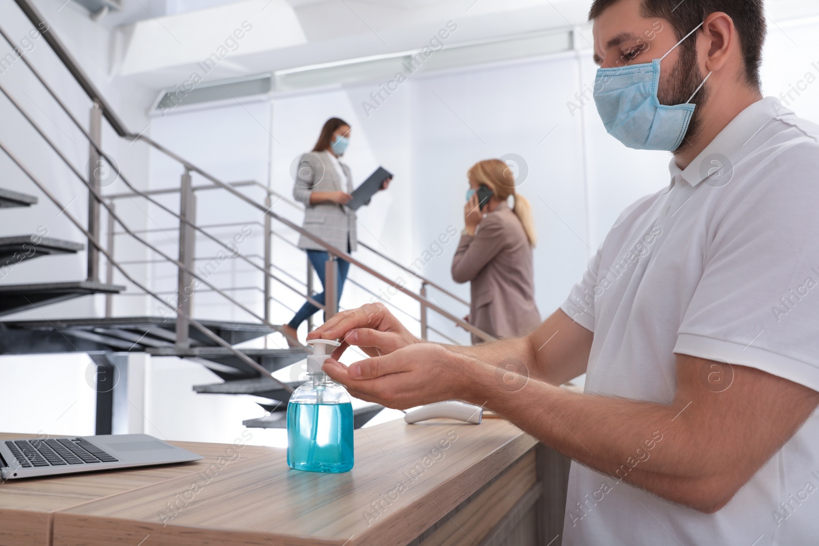 Photo of Man applying hand sanitizer at office reception