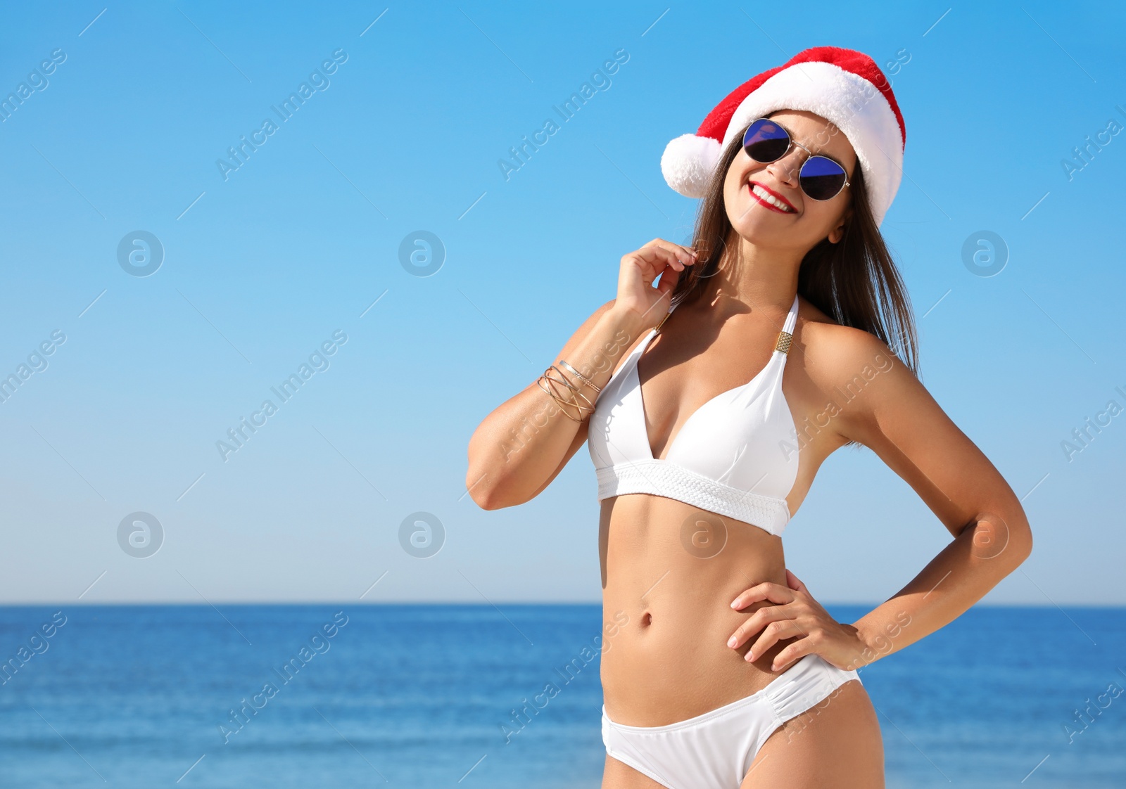 Photo of Young woman wearing Santa hat and bikini on beach, space for text. Christmas vacation