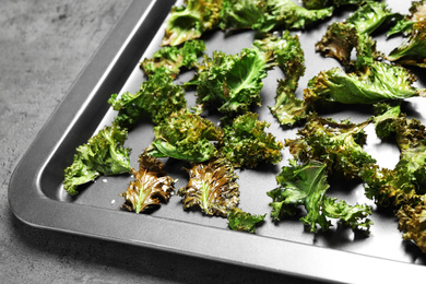 Tasty kale chips with seeds on baking sheet, closeup