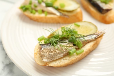 Photo of Delicious sandwiches with sprats, pickled cucumber, green onion and dill on plate, closeup