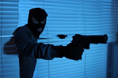 Thief with gun coming out of blinds at night. Burglary