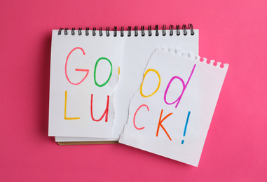 Photo of Torn phrase GOOD LUCK written in notebook on pink background, top view