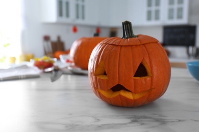 Photo of Pumpkin jack o'lantern on white marble table in kitchen, space for text. Halloween celebration
