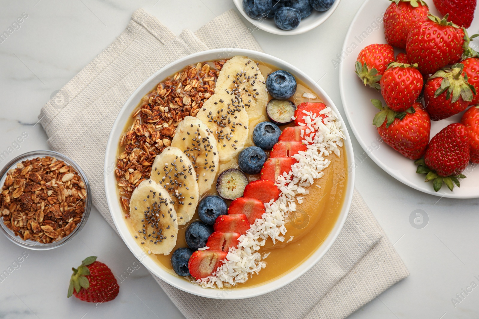 Photo of Delicious smoothie bowl with fresh berries, banana, coconut flakes and granola on white table, flat lay