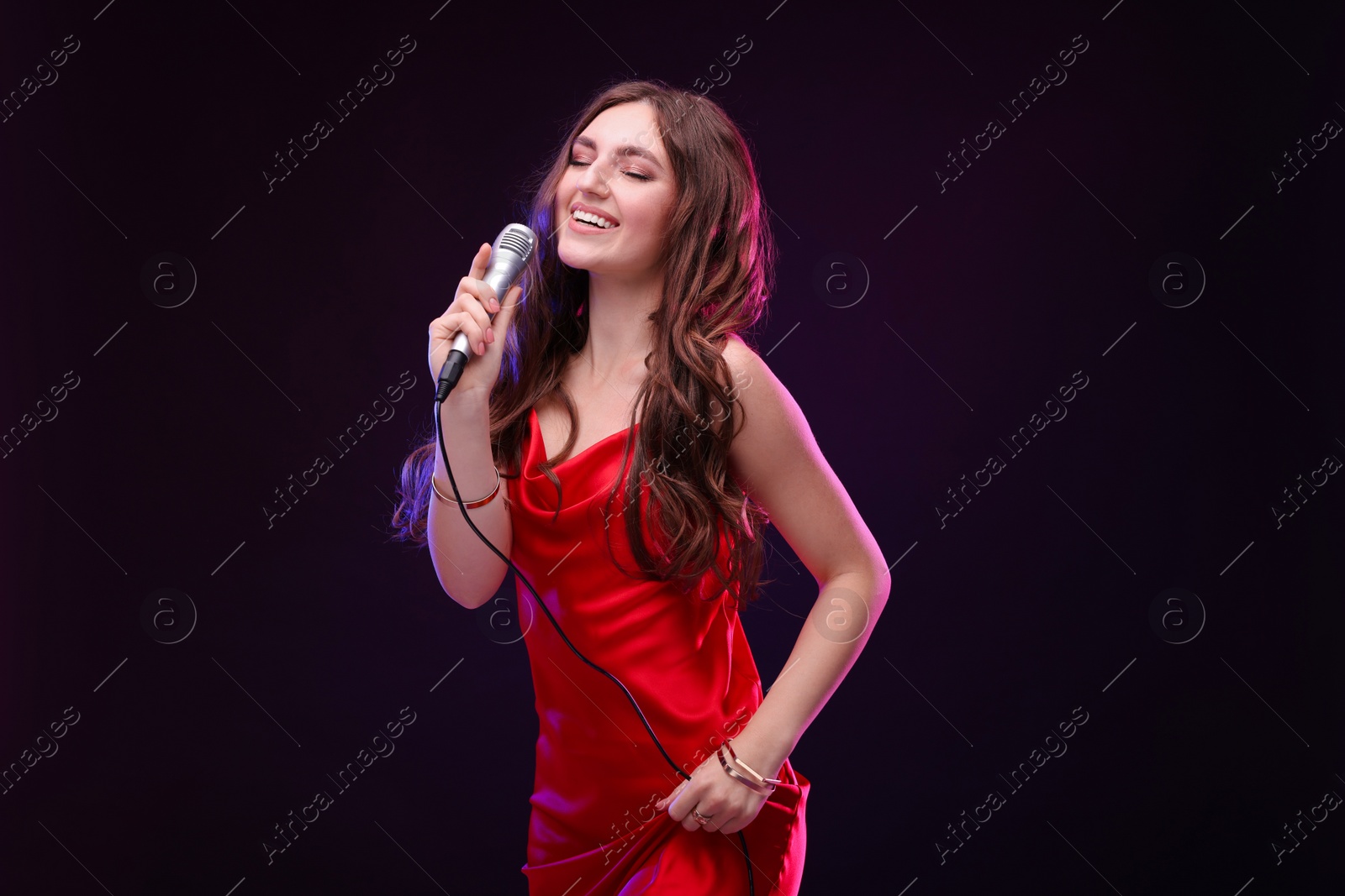 Photo of Happy woman with microphone singing in color light on black background