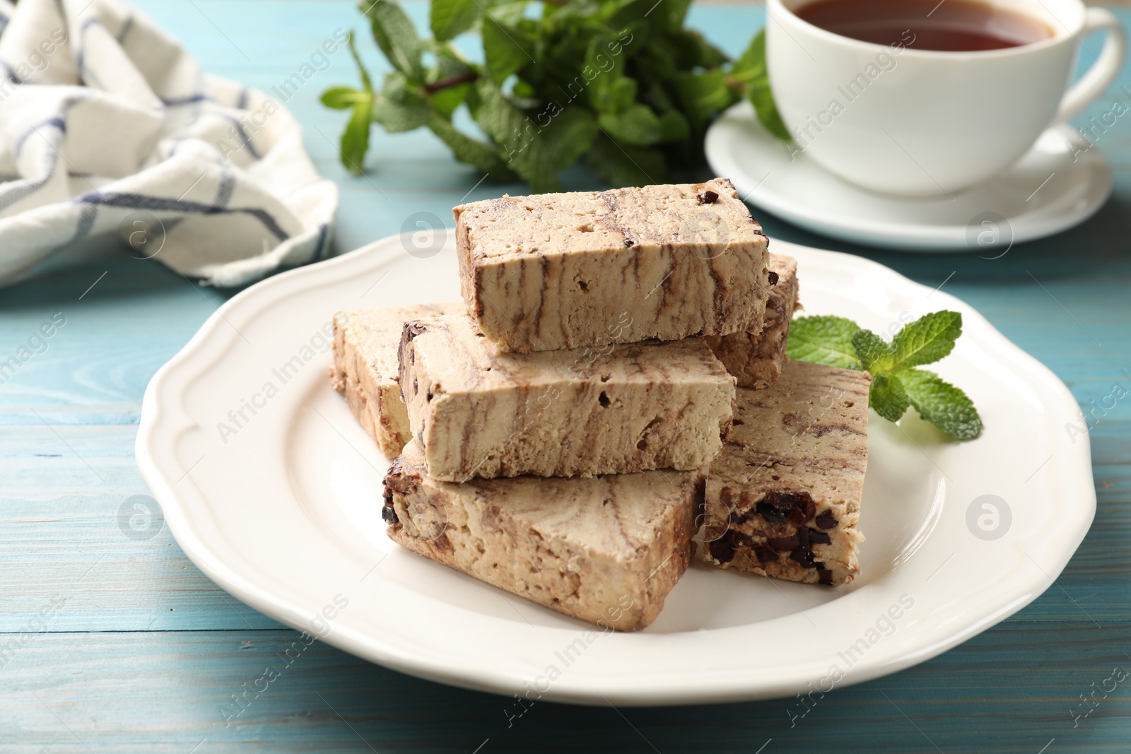 Photo of Pieces of tasty chocolate halva and mint served on light blue wooden table, closeup