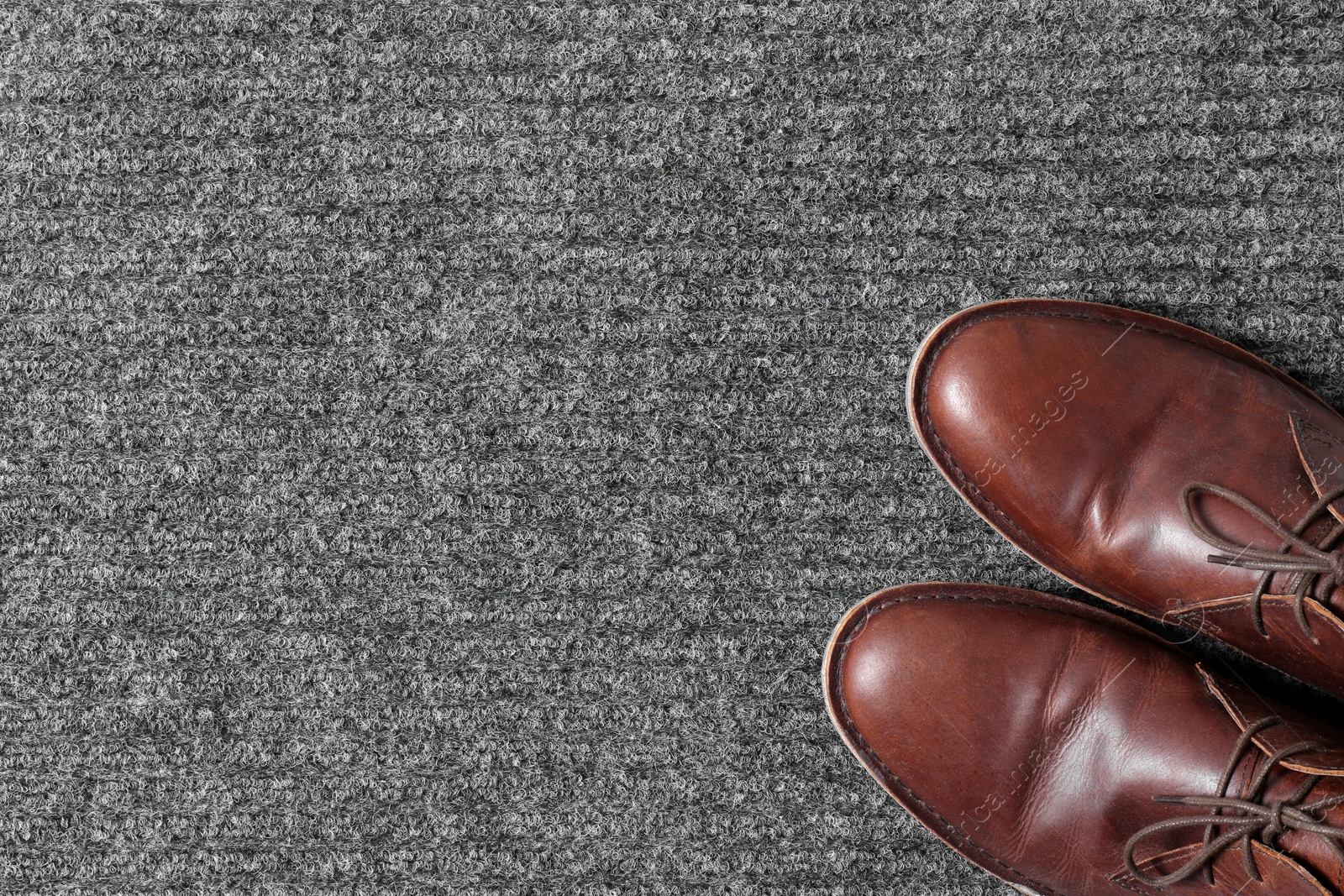 Photo of Brown classic shoes on gray doormat, top view. Space for text