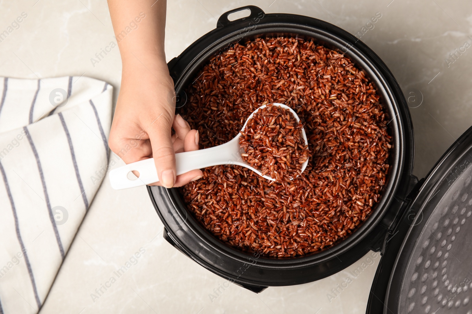 Photo of Woman taking delicious brown rice from multi cooker at table, top view