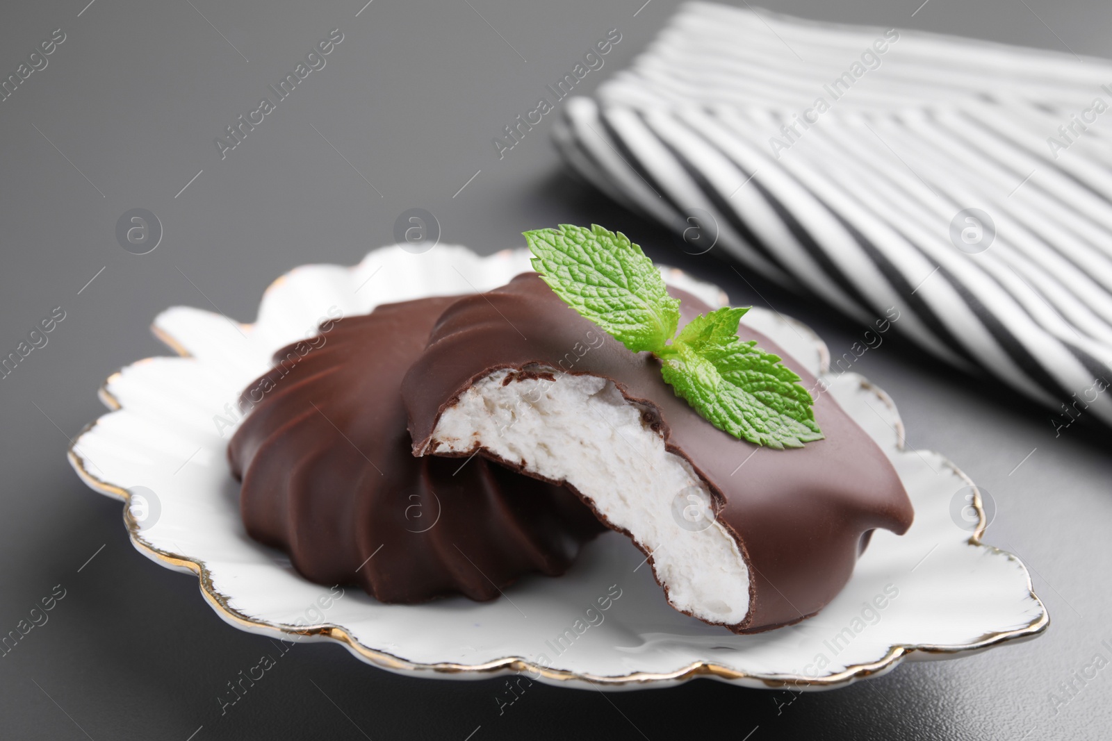 Photo of Delicious chocolate covered zephyrs with mint on black table, closeup