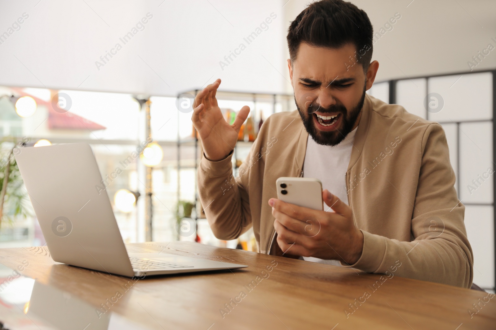 Photo of Emotional young man with smartphone at table in office. Online hate concept