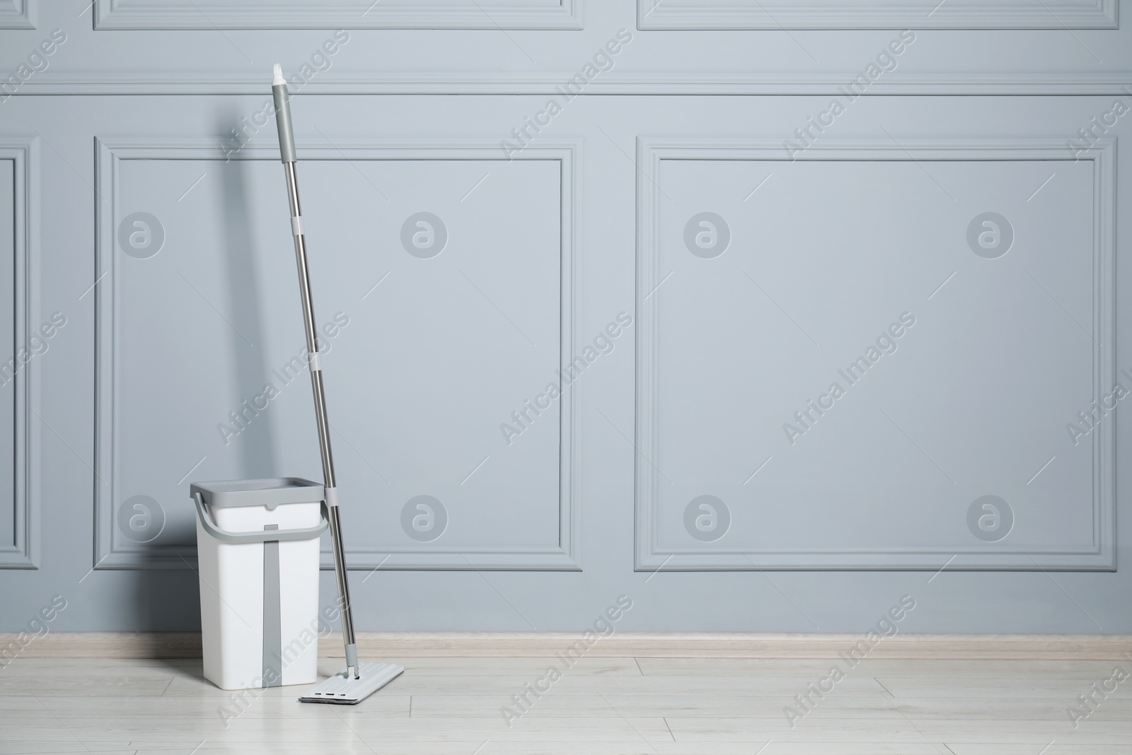 Photo of Mop and bucket on parquet near grey wall indoors, space for text. Cleaning floor