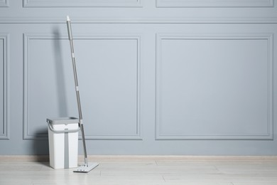 Mop and bucket on parquet near grey wall indoors, space for text. Cleaning floor