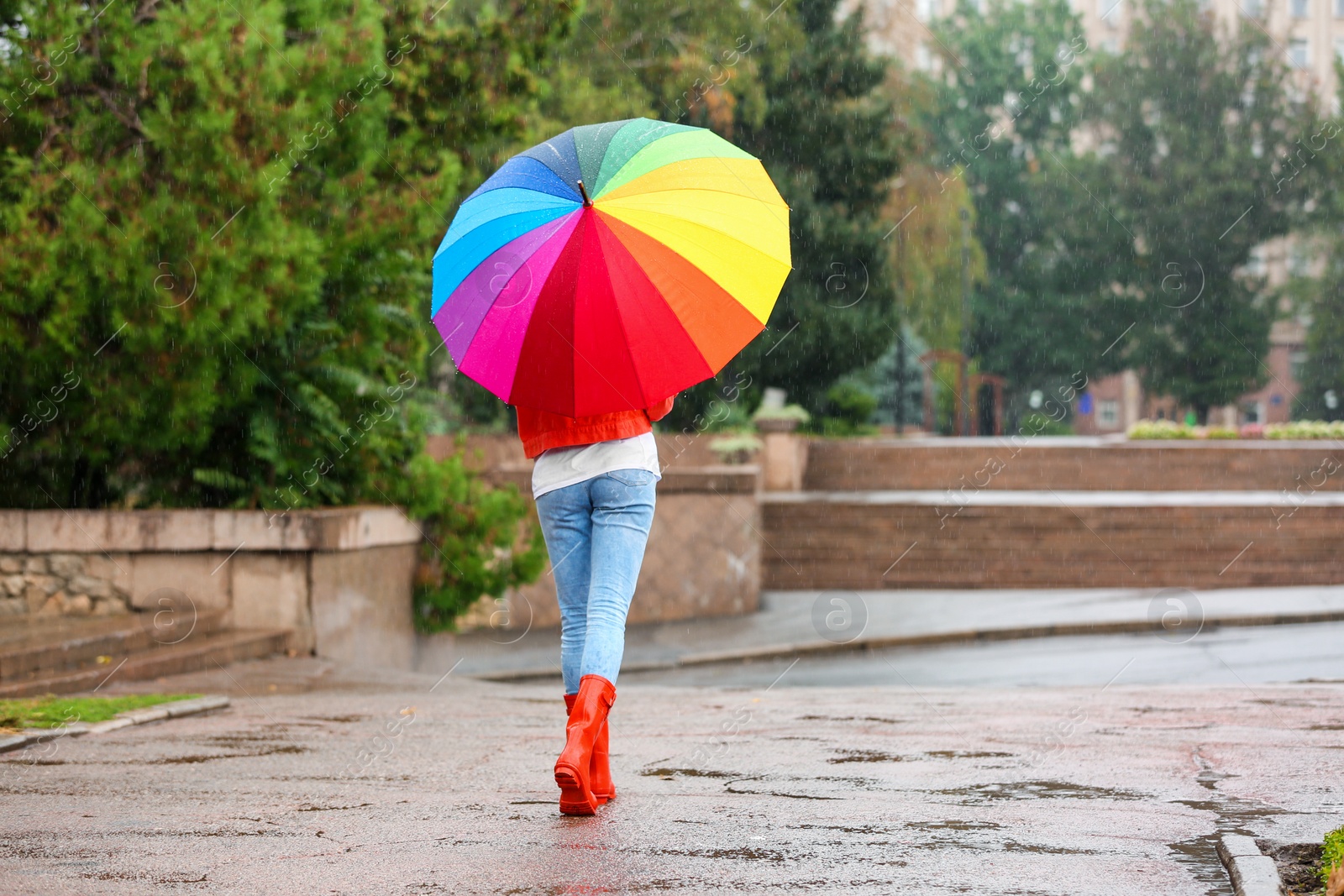 Photo of Young woman with bright umbrella under rain outdoors