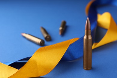 Ribbons in colors of national Ukrainian flag and bullets on blue background, closeup. Space for text