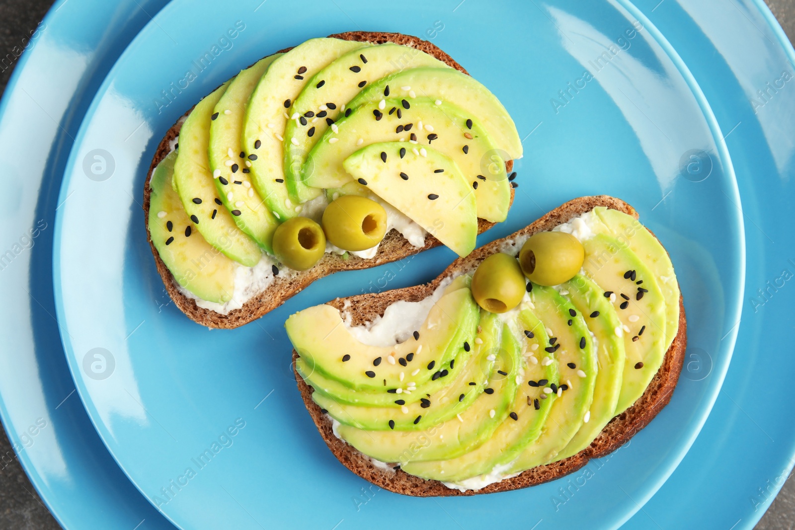 Photo of Crisp rye toasts with avocado, cream cheese and olives on plate, top view