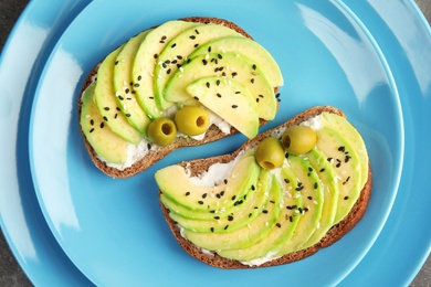 Crisp rye toasts with avocado, cream cheese and olives on plate, top view