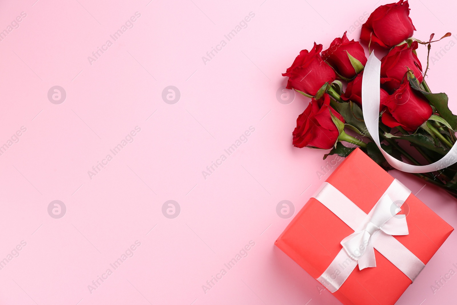 Photo of Beautiful red roses and gift box on pink background, flat lay with space for text. Valentine's Day celebration