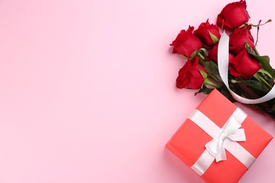 Beautiful red roses and gift box on pink background, flat lay with space for text. Valentine's Day celebration