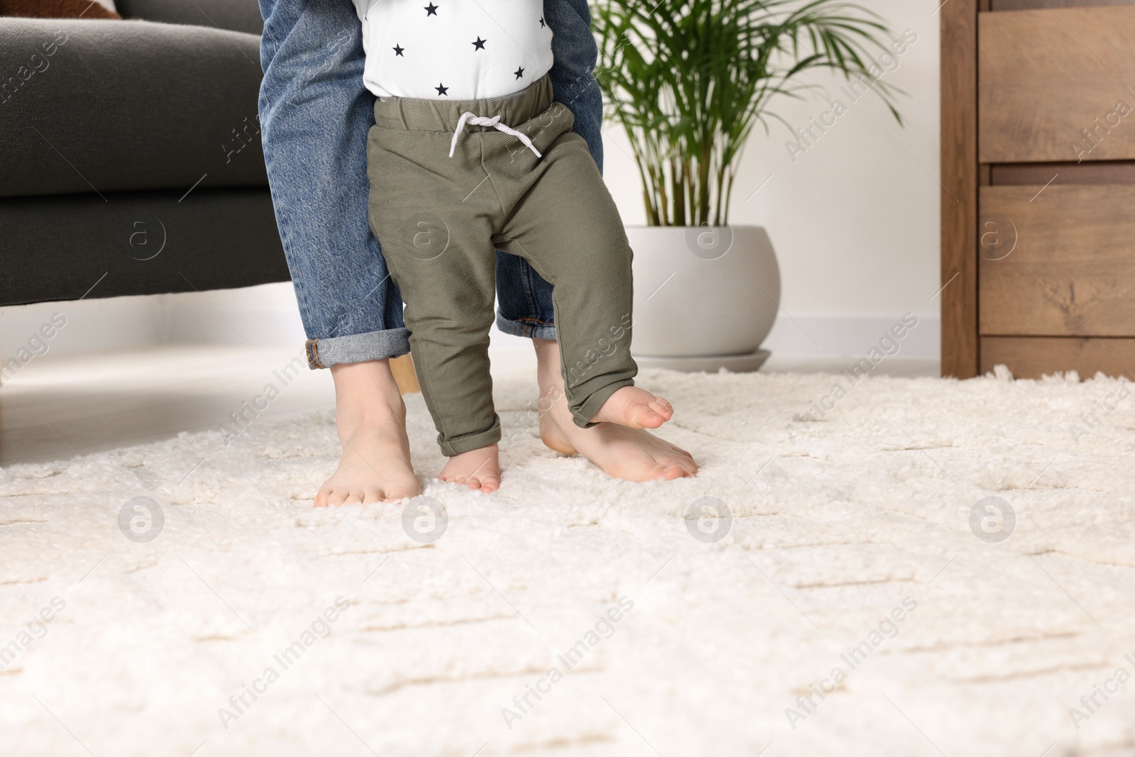 Photo of Mother supporting her baby son while he learning to walk on carpet at home, closeup