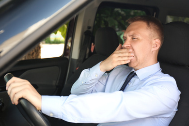 Photo of Tired young man yawning in his car